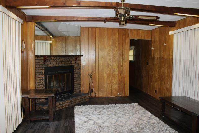 living area featuring beam ceiling, a brick fireplace, wood walls, a ceiling fan, and wood finished floors
