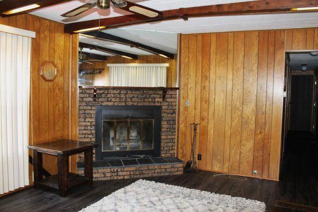living area with a ceiling fan, a brick fireplace, wood walls, wood finished floors, and beamed ceiling