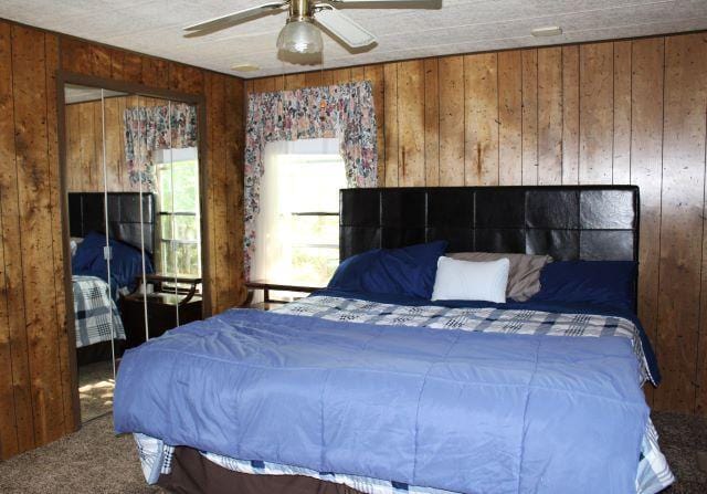 carpeted bedroom featuring a ceiling fan and wooden walls