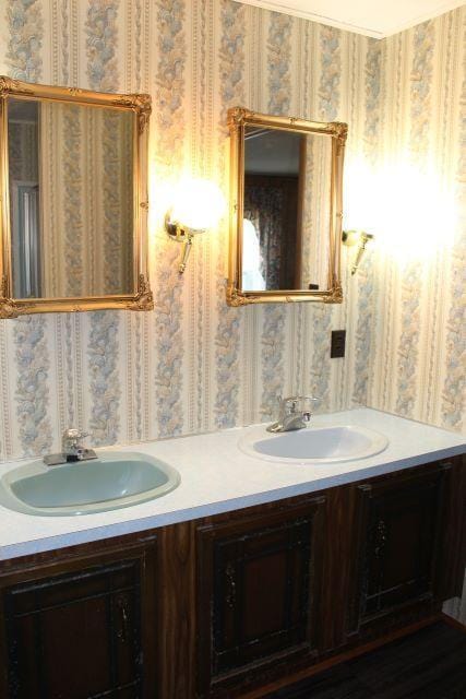 full bath with double vanity, wallpapered walls, and a sink