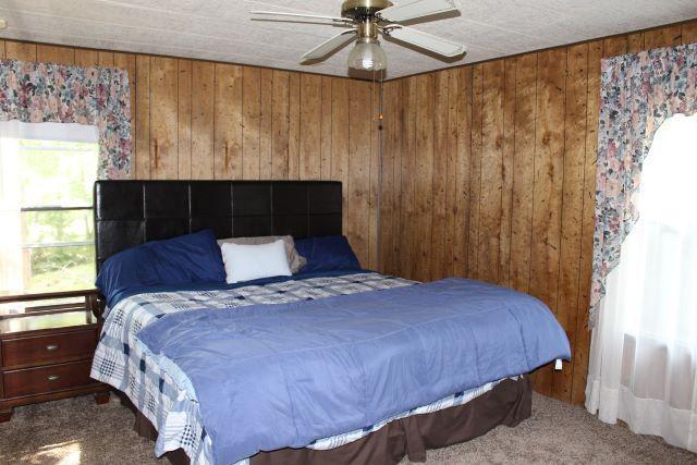 carpeted bedroom featuring ceiling fan and wood walls