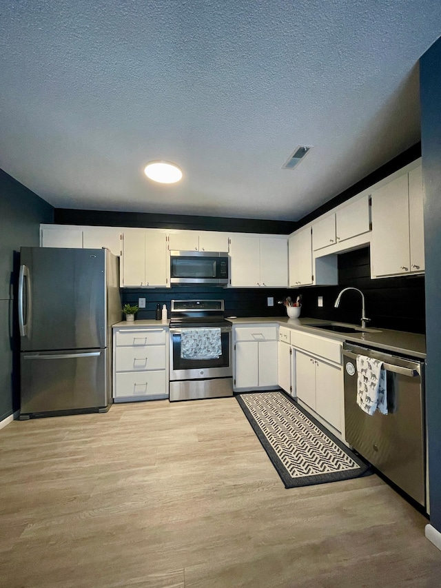 kitchen featuring appliances with stainless steel finishes, a sink, visible vents, and light wood-style floors