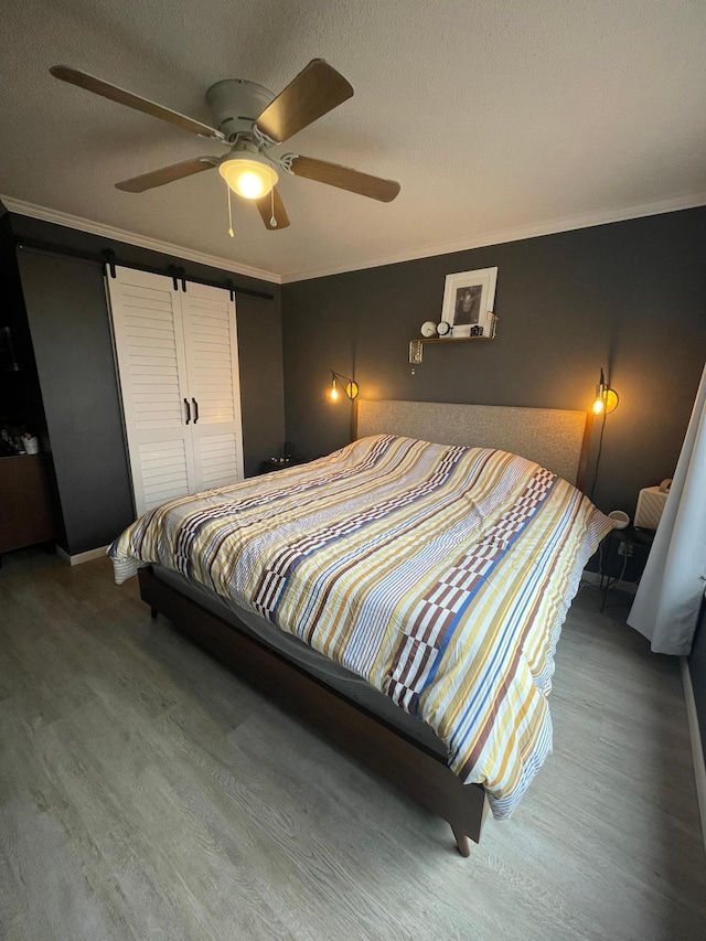 bedroom featuring a ceiling fan, a barn door, wood finished floors, baseboards, and ornamental molding