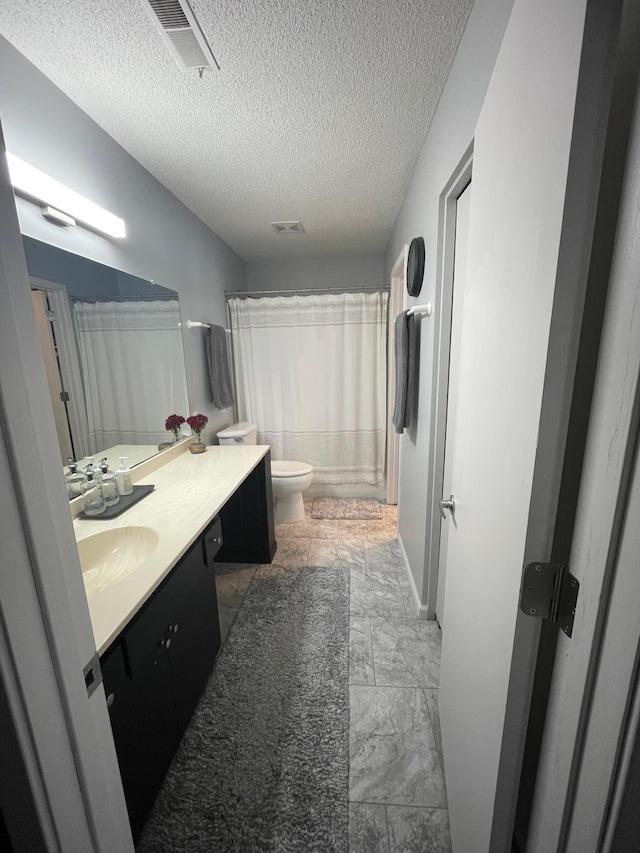 full bath with a textured ceiling, visible vents, vanity, toilet, and marble finish floor