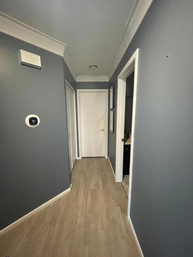 hallway with baseboards, ornamental molding, a textured ceiling, and wood finished floors
