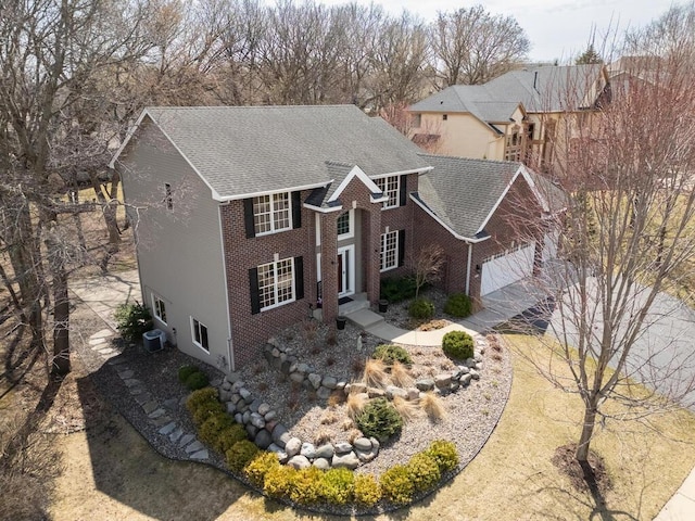 colonial inspired home featuring a shingled roof, an attached garage, cooling unit, and brick siding