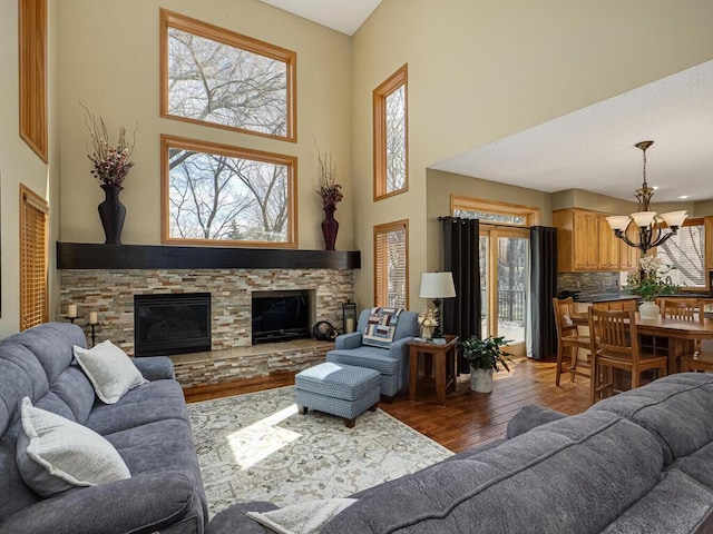 living area with a fireplace, a chandelier, wood finished floors, and a towering ceiling