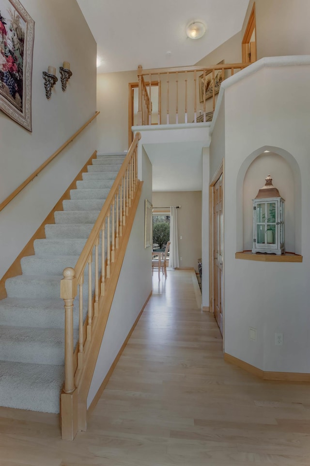 hallway featuring stairway, baseboards, wood finished floors, and a towering ceiling