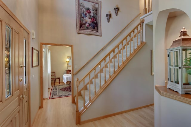 entryway with light wood-type flooring, baseboards, a high ceiling, and stairway