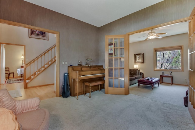 living area with baseboards, carpet, stairs, and ceiling fan