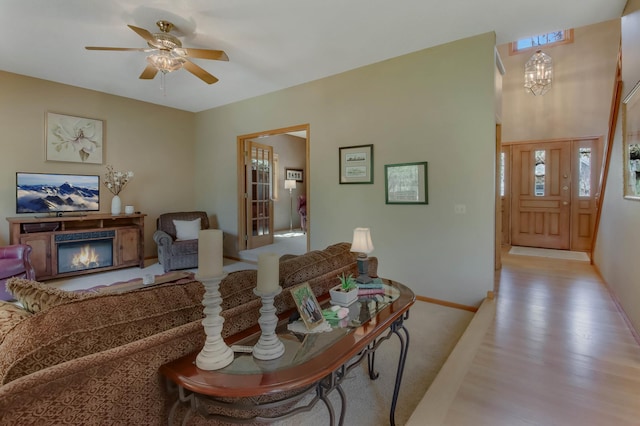 living area featuring ceiling fan, baseboards, a glass covered fireplace, and light wood-style flooring