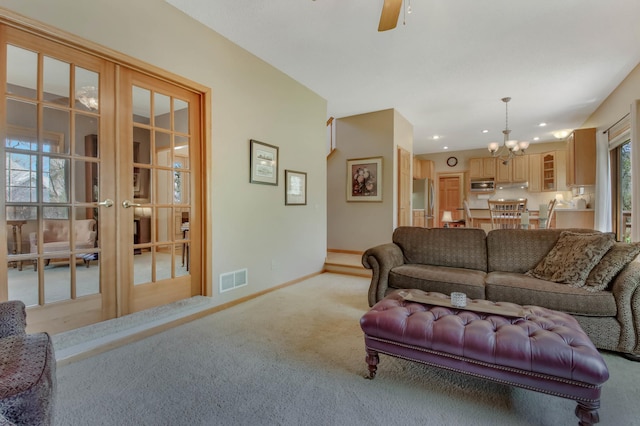 living area with french doors, visible vents, baseboards, ceiling fan with notable chandelier, and light carpet
