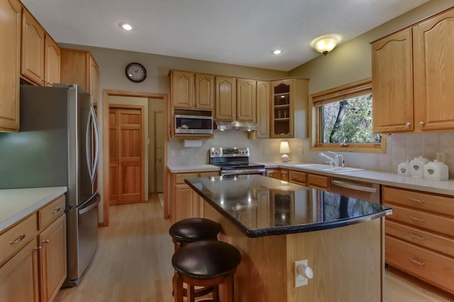 kitchen with a breakfast bar, a sink, light wood-style flooring, stainless steel appliances, and under cabinet range hood