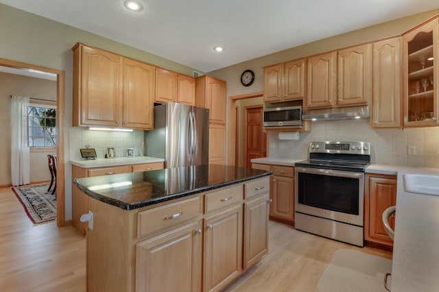 kitchen with light brown cabinets, light wood-type flooring, under cabinet range hood, tasteful backsplash, and stainless steel appliances