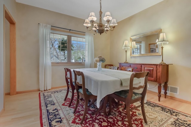 dining space featuring baseboards, light wood finished floors, a notable chandelier, and visible vents