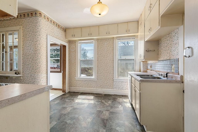 kitchen featuring a sink, baseboards, wallpapered walls, and light countertops