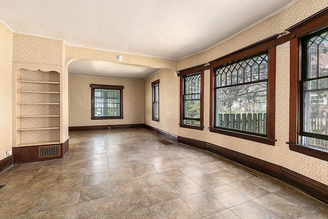 empty room with crown molding, wallpapered walls, visible vents, and baseboards