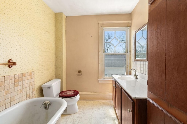 bathroom with vanity, toilet, baseboards, wallpapered walls, and a freestanding bath