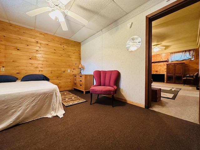 bedroom with wooden walls, a ceiling fan, a paneled ceiling, and carpet