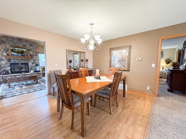 dining space with a fireplace, baseboards, a chandelier, and light wood-style floors