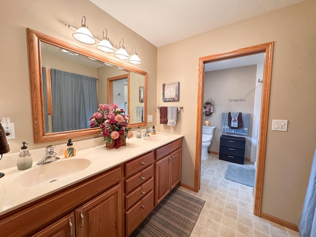 bathroom with double vanity, toilet, a textured ceiling, and a sink