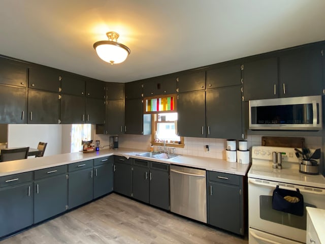 kitchen with light wood-type flooring, light countertops, a sink, appliances with stainless steel finishes, and backsplash
