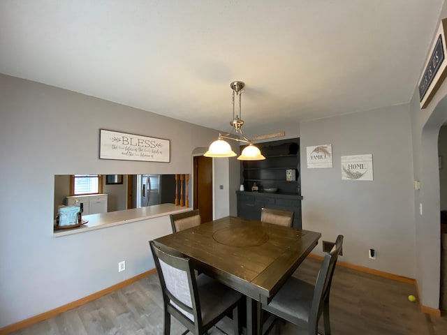 dining space featuring arched walkways, baseboards, and wood finished floors