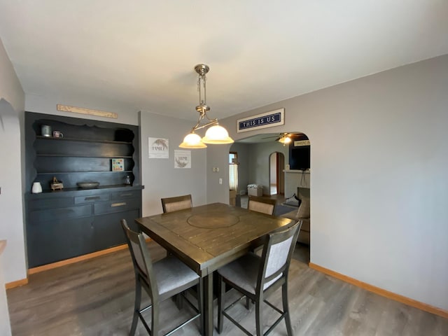 dining area with baseboards, arched walkways, a ceiling fan, and wood finished floors