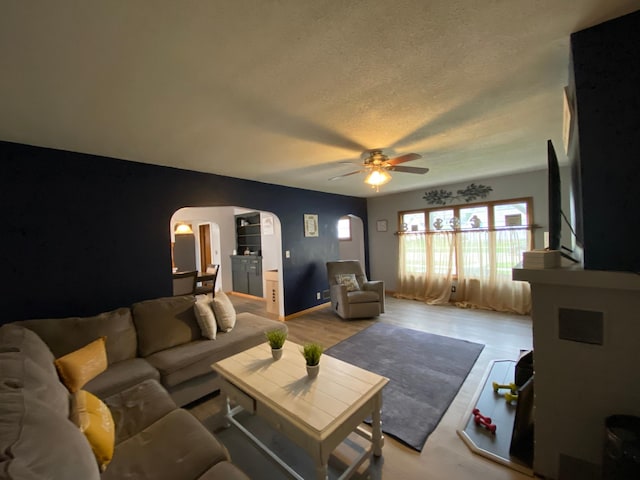 living area featuring arched walkways, a textured ceiling, ceiling fan, and light wood finished floors