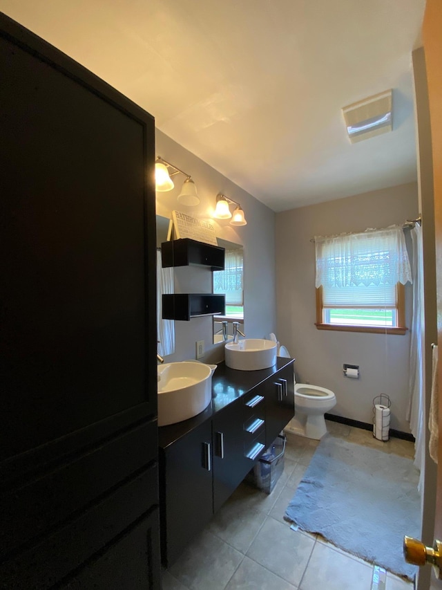 bathroom featuring tile patterned flooring, double vanity, a sink, and toilet