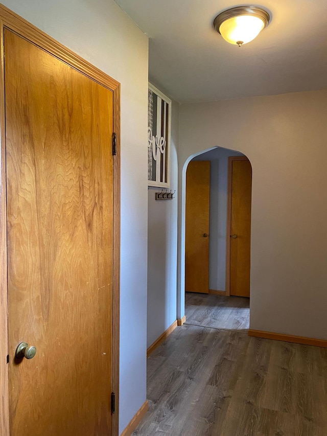 hallway featuring arched walkways, baseboards, and wood finished floors