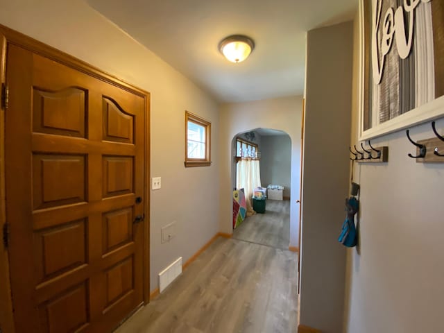 foyer featuring arched walkways, baseboards, visible vents, and light wood-style floors