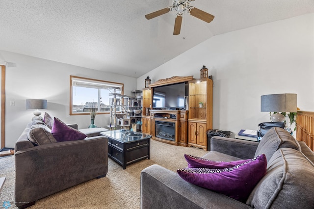 living room featuring a ceiling fan, a textured ceiling, vaulted ceiling, a glass covered fireplace, and carpet flooring