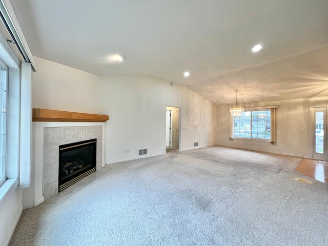 unfurnished living room with light colored carpet, a fireplace, a chandelier, vaulted ceiling, and visible vents
