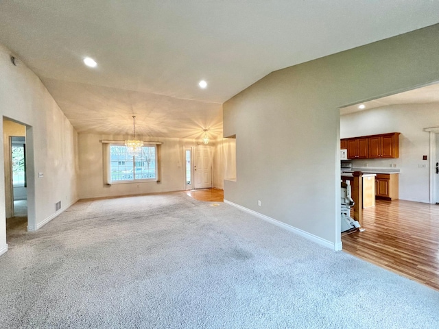 unfurnished living room with vaulted ceiling, baseboards, a notable chandelier, light carpet, and recessed lighting