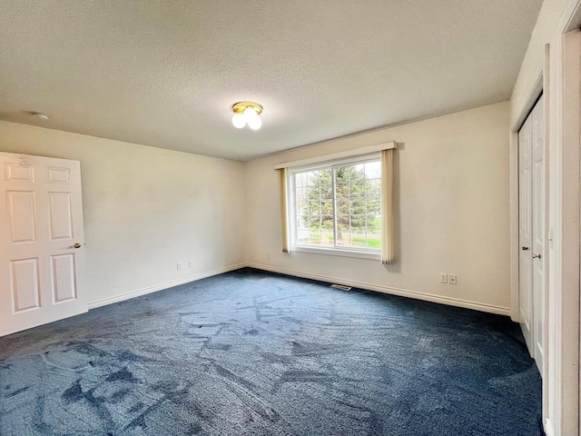 unfurnished bedroom featuring a textured ceiling, baseboards, and dark colored carpet