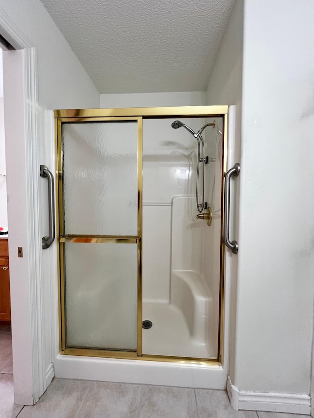 bathroom with a textured ceiling, tile patterned floors, and a shower stall