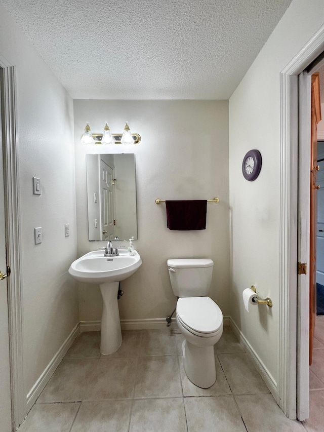 bathroom featuring toilet, tile patterned floors, baseboards, and a textured ceiling