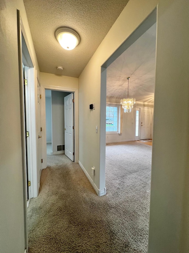 hall featuring an inviting chandelier, visible vents, baseboards, a textured ceiling, and carpet flooring