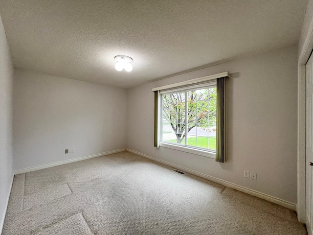 carpeted spare room featuring visible vents, a textured ceiling, and baseboards