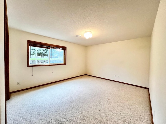 spare room featuring light colored carpet, a textured ceiling, and baseboards