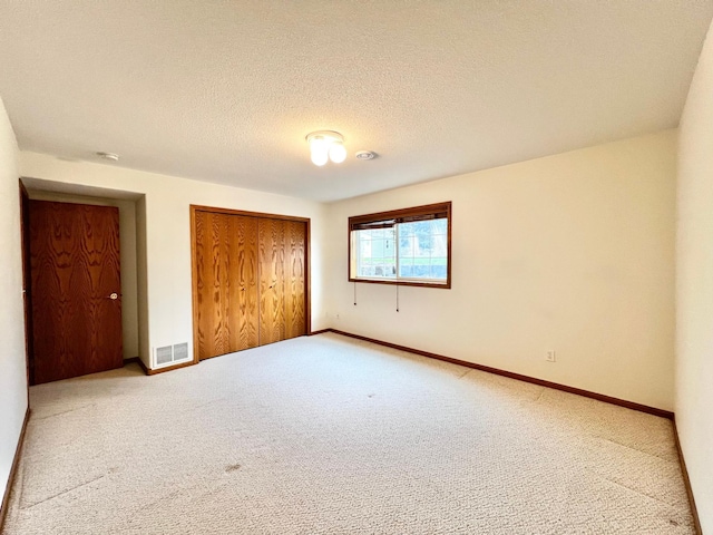 unfurnished bedroom with a textured ceiling, visible vents, baseboards, a closet, and carpet