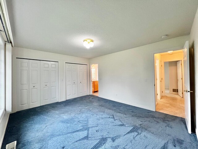 1647 8th Ave, Granite Falls, MN 56241 - unfurnished bedroom with a textured ceiling, dark colored carpet, two closets, baseboards, and visible vents