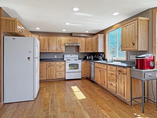 kitchen featuring dark countertops, white appliances, light wood-style floors, under cabinet range hood, and a sink