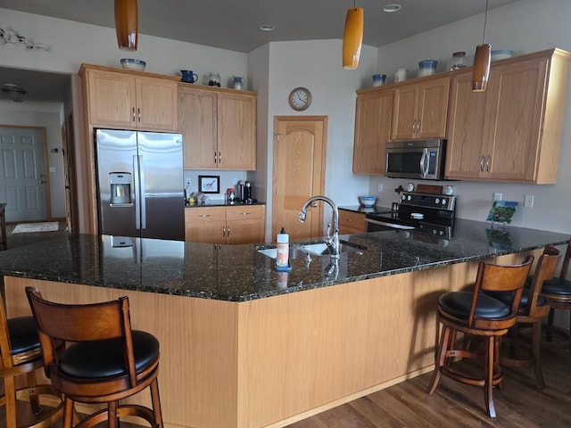 kitchen featuring a sink, a peninsula, stainless steel appliances, dark stone countertops, and dark wood-style flooring