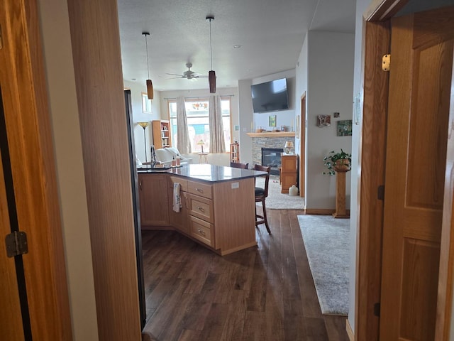 kitchen with a breakfast bar, dark wood finished floors, ceiling fan, open floor plan, and a stone fireplace