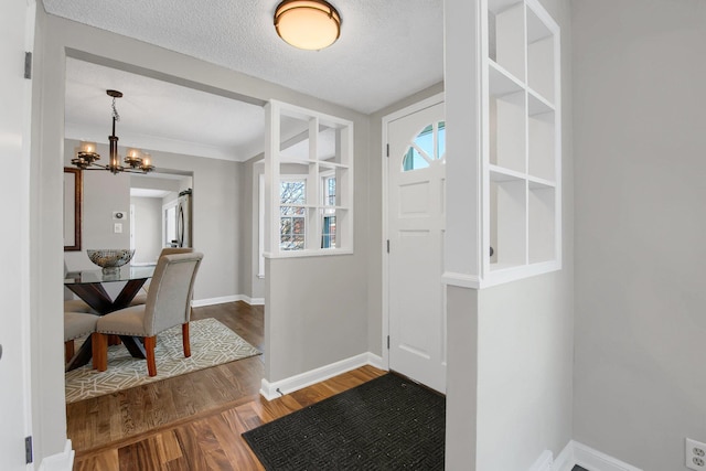 foyer entrance with a textured ceiling, baseboards, a chandelier, and wood finished floors