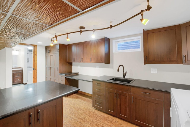 kitchen with independent washer and dryer, dark countertops, a sink, and light wood-style floors