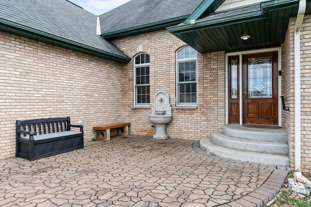 doorway to property featuring a shingled roof and brick siding