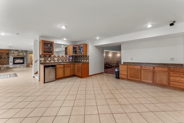 kitchen with stainless steel dishwasher, brown cabinetry, tasteful backsplash, and a fireplace